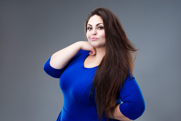 Fototapeta na wymiar Brunette plus size fashion model in blue dress, fat woman with long hair on gray background