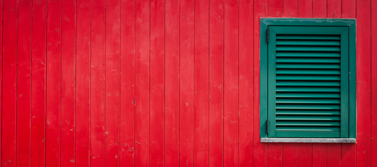 red wooden wall with a green shutter on the right 