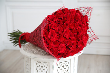 A large bouquet of red roses on a carved nightstand in a bright interior.
