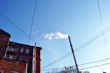 Old pipe with smoke, red brick building corner with windows and wires on winter bright blue sky background, view from ground on top