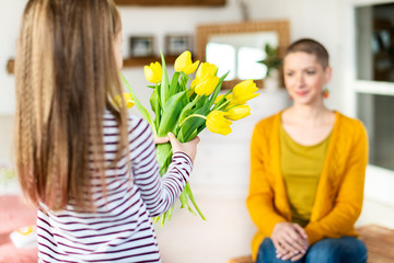Happy Mother's Day or Birthday Background. Adorable young girl surprising her mom with bouquet of yellow tulips. Family celebration concept.