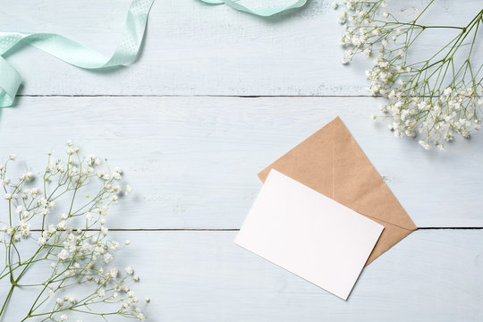  Kraft envelope and blank card on blue wooden desk with flowers. Empty greeting card for your congratulation with Easter, Mother or Womans day, spring background, 