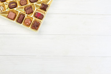 Different chocolate candies in box. Assortment of chocolate candies in golden box on white wooden background with copy space.