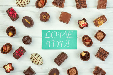 Valentines Day background with sweets. Assorted chocolate candies and Valentines Day card on white background, top view. Concept of love confession.