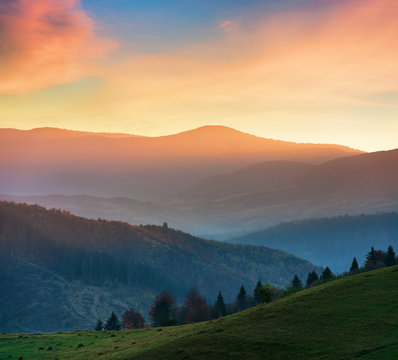 beautiful autumn scenery in mountains at sunset. red clouds on the sky, blue shade in the mountains, grassy green meadow.