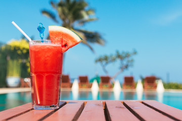 Healthy concept, Water melon smoothie on a wood table with swimming pool and blue sky background.