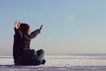 a man sits on an ice and looks at the sun with his arms raised to the side up