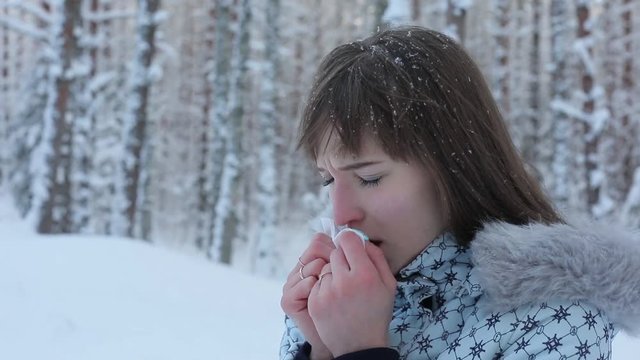 A young woman coughing in a winter park. You need to apply pills. The trees are covered with snow.