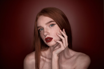 The portrait of a young redhead lady isolated over a red background