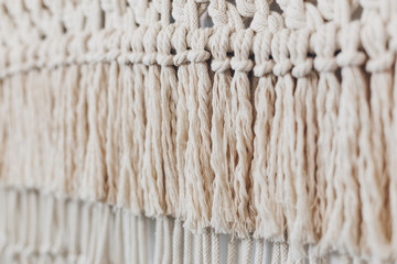 Detail of cream macrame decor displayed hanging on a wall.