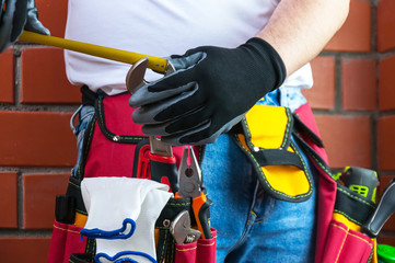 Fototapeta premium Tools in the belt for tools. The builder measures the diameter of the key with a tape measure. Selective focus.