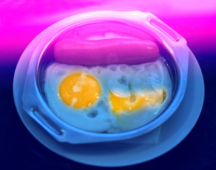 Delicious sausage with fried eggs in an iron bowl