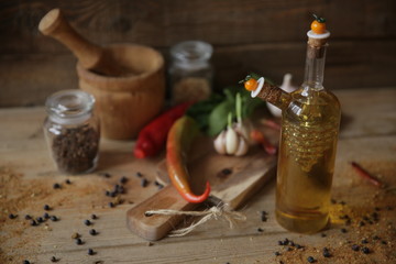 olive oil in a bottle on a wooden background with a wooden board with garlic, spices, dried pepper and herbs for decoration