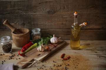 olive oil in a bottle on a wooden rustic background with a wooden board with garlic, dried pepper and herbs for decoration. With copy space for text.