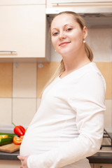 Portrait of Happy Smiling Pregnant Female Posing Against Cut Fresh Vegetables on Chopping Board at Kitchen.
