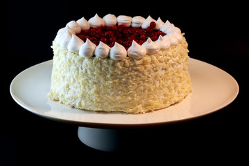 Tasty little white cake with nuts and red berries on white dish.