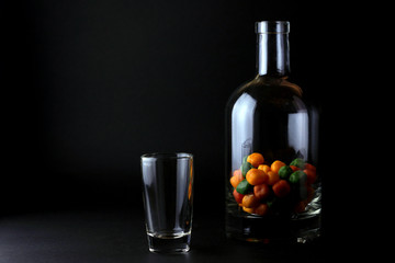 Small round colorful candies pour in bottle on black background. Sweet drink concept.