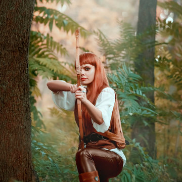 new image of Robin Hood as girl hunter, attractive lady in white shirt and leather pants pulled bow before shot at target, confident earner with red hair prepared arrow, bright photo in green forest
