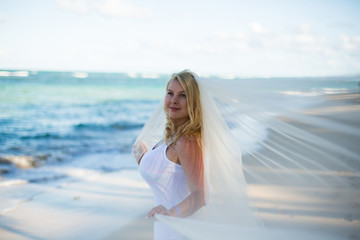 Young sexy blonde woman in white dress and bridal veil near sea. Girl at the beach