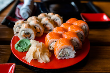 sushi restaurant menu, delicious japanese traditional seafood. gourmet maki roll with tamago omelet, chuka and cream cheese, covered with salmon, served on red plate, close up