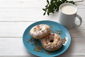 Donuts on a blue plate with a cup of milk on a white wooden background