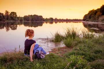 Fototapeta premium A young girl on the river bank admires nature during the sunset_