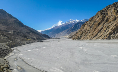 Barren and desolate landscape. Harsh and steep slopes of high mountains. Endless road to walk. Snowy peaks in the back. River bank has completely dried out. Himalayas, Annapurna Circuit trek in Nepal.
