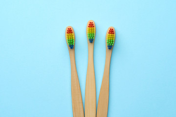 Image of three wooden toothbrushes with rainbow-colored bristles.
