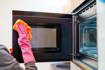 Image of woman hands in rubber gloves washing microwave.