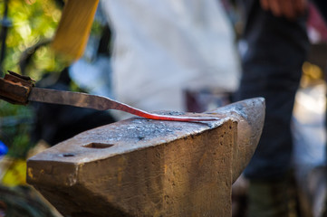 blacksmith performs the forging of hot glowing metal on the anvil