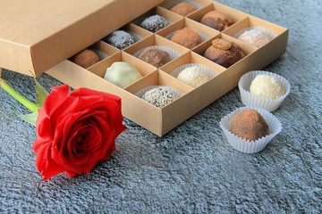 Chocolate candies in a box and a rose are on a gray background