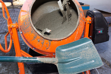 construction worker shovels the sand into the concrete mixer. process of creating cement on the...