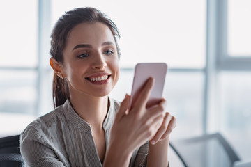 Young business woman on the phone at office. Business woman texting on the phone. Pretty young business woman sitting in the workplace.