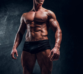 Fototapeta na wymiar Athletic man with muscular body wearing underwear. Cropped photo in a studio with dark wall background 