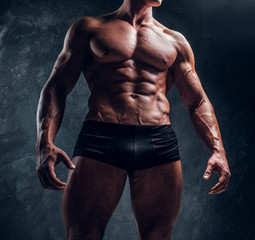 Athletic man with muscular body wearing underwear. Cropped photo in a studio with dark wall...