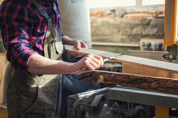 The worker makes measurements of a wooden board with corner ruler.