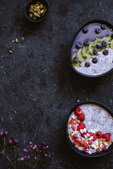 Healthy breakfast bowls with coconut yogurt, fruits, berries and pistachios on black background top view. With copy space
