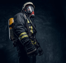 Naklejka premium Firefighter in safety helmet and oxygen mask wearing protective clothes. Studio photo against a dark textured wall 