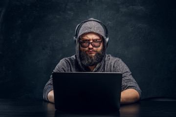 A hacker sits behind a laptop in a dark room and stares intently at the camera