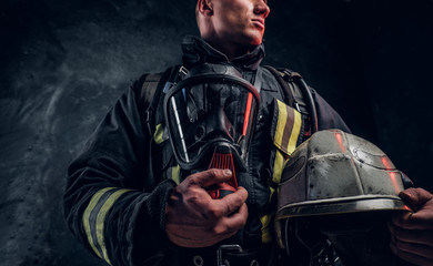 Low angle photo of a man wearing a fire suit holding an oxygen mask and helmet, looking sideways....