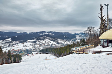 Panorama of ski resort, slope, people on the ski lift, skiers on the piste among green pine trees...