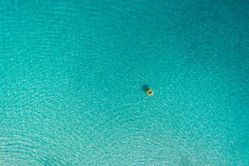 Fototapeta na wymiar Aerial view of slim woman swimming on the swim ring donut in the transparent turquoise sea in Seychelles. Summer seascape with girl, beautiful waves, colorful water. Top view from drone