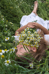 Beautiful little girl in a white dress is lying on a green meadow with a bouquet of daisies
