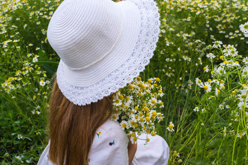 Portrait of a beautiful girl in a white hat and with a bouquet of daisies on a flower meadow background