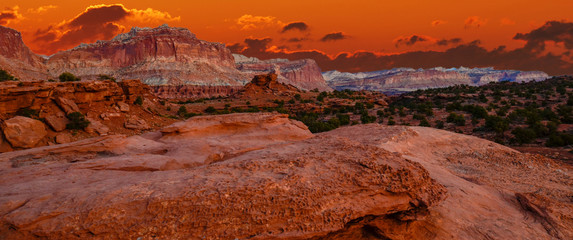 Fototapeta na wymiar Sunset during golden hour in Southern Utah, sun warming red sandstone, cliffs, mountains, and mesa. With orange sky and red clouds