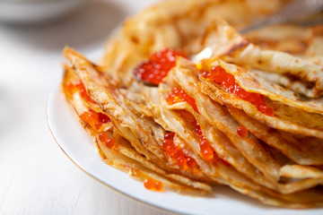 A stack of thin russian pancakes with caviar on a white plate