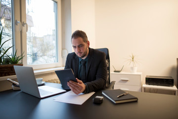 businessman working on laptop in office taking notes on tablet