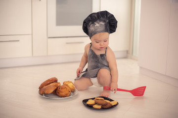 a small child cook in a white kitchen in a black cap and an apron cooking dough and flour baby food