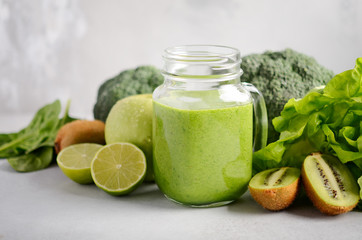 Fresh green smoothie in a jar with ingredients on a gray concrete background, selective focus.