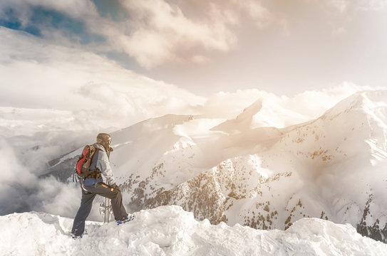 Snowboarder stay with snowboard in hands sits on big rock on mountains backdrop. Bansko, Bulgaria